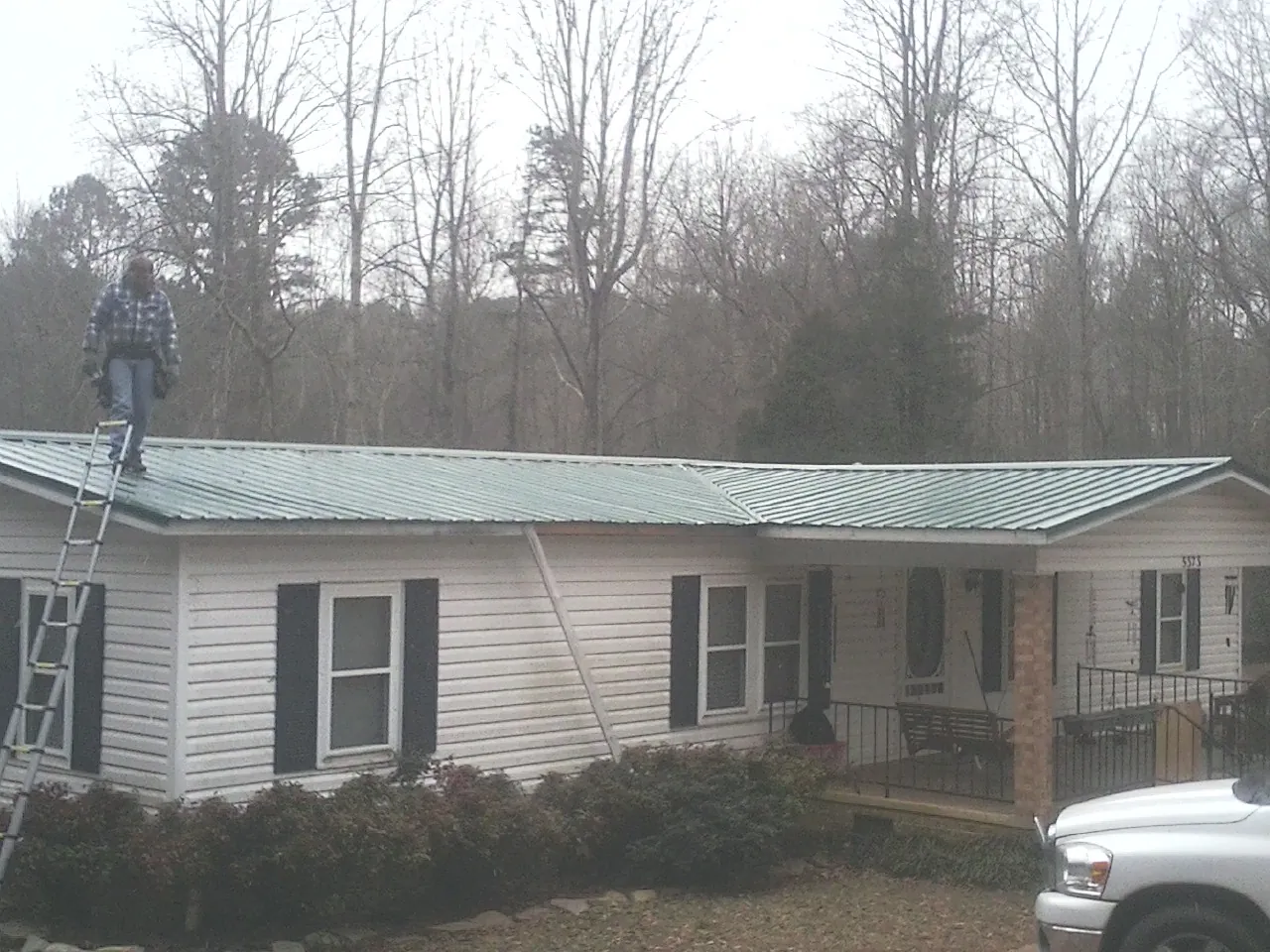 Worker on a ladder beside a new green metal roof on a ranch home in Rutland