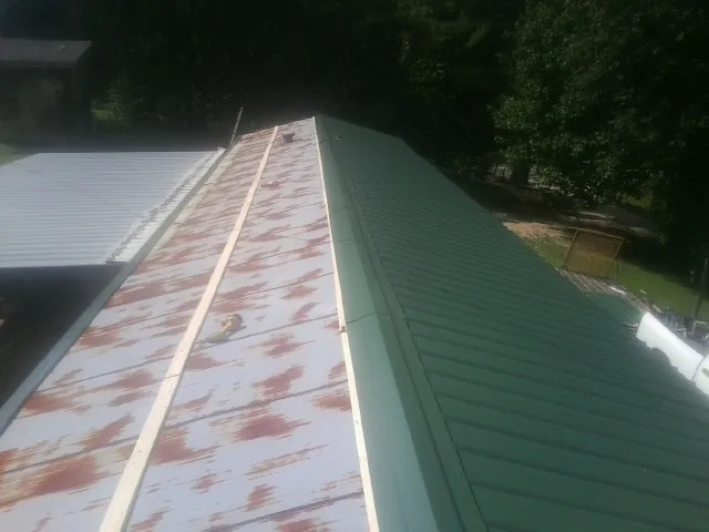 Old rusted panels beside newly installed green metal roofing — Wind Damage Roof Repair by Roofing Brothers in Rutland